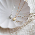 Two necklaces with pendants on a white shell and beige fabric background