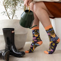Person wearing colorful socks with a plant and black boots on a light wooden floor.