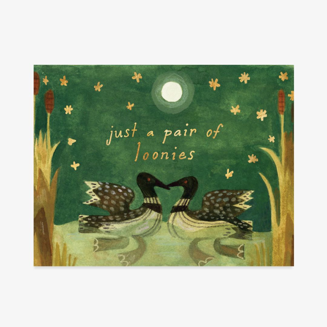A square art print or card featuring an illustrated green woodland scene with two loons facing each other, small yellow flowers, reeds, and the text 'just a pair of loonies' in a light cream font.