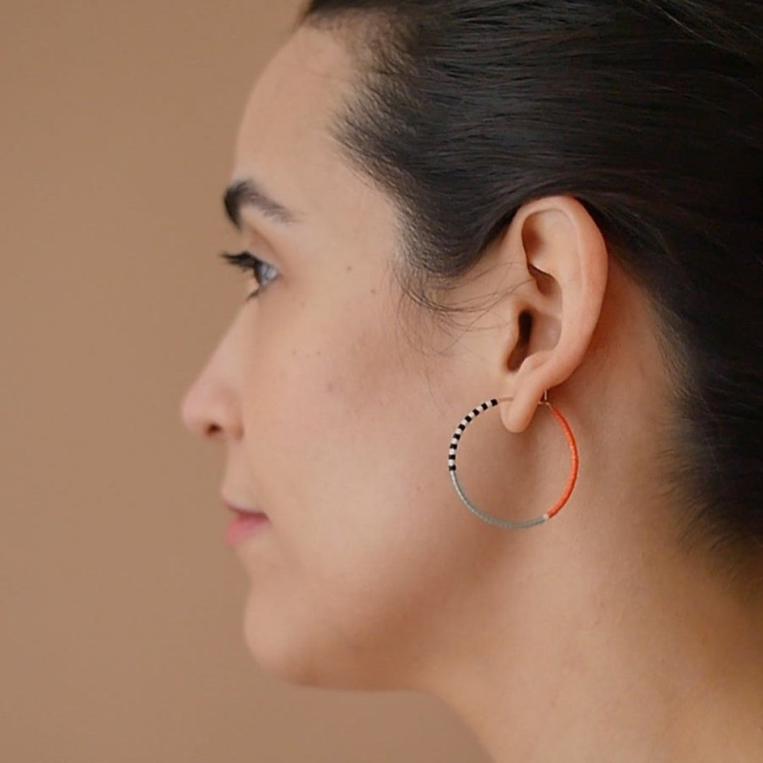 A pair of delicate 14 KT gold hoop earrings, each partially threaded with small Japanese glass seed beads in a pattern of light blue, white, black, and coral. The beads cover approximately half of each hoop, leaving the remaining gold wire visible.