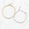 Two bracelets on a white surface. One bracelet is gold-colored, and the other is silver-colored. Both bracelets have a chain link design made of small, rectangular links.