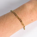 Gold chain bracelet on a wrist with a plain background