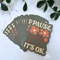 Stack of stickers with floral design and text on a white surface with leaves.