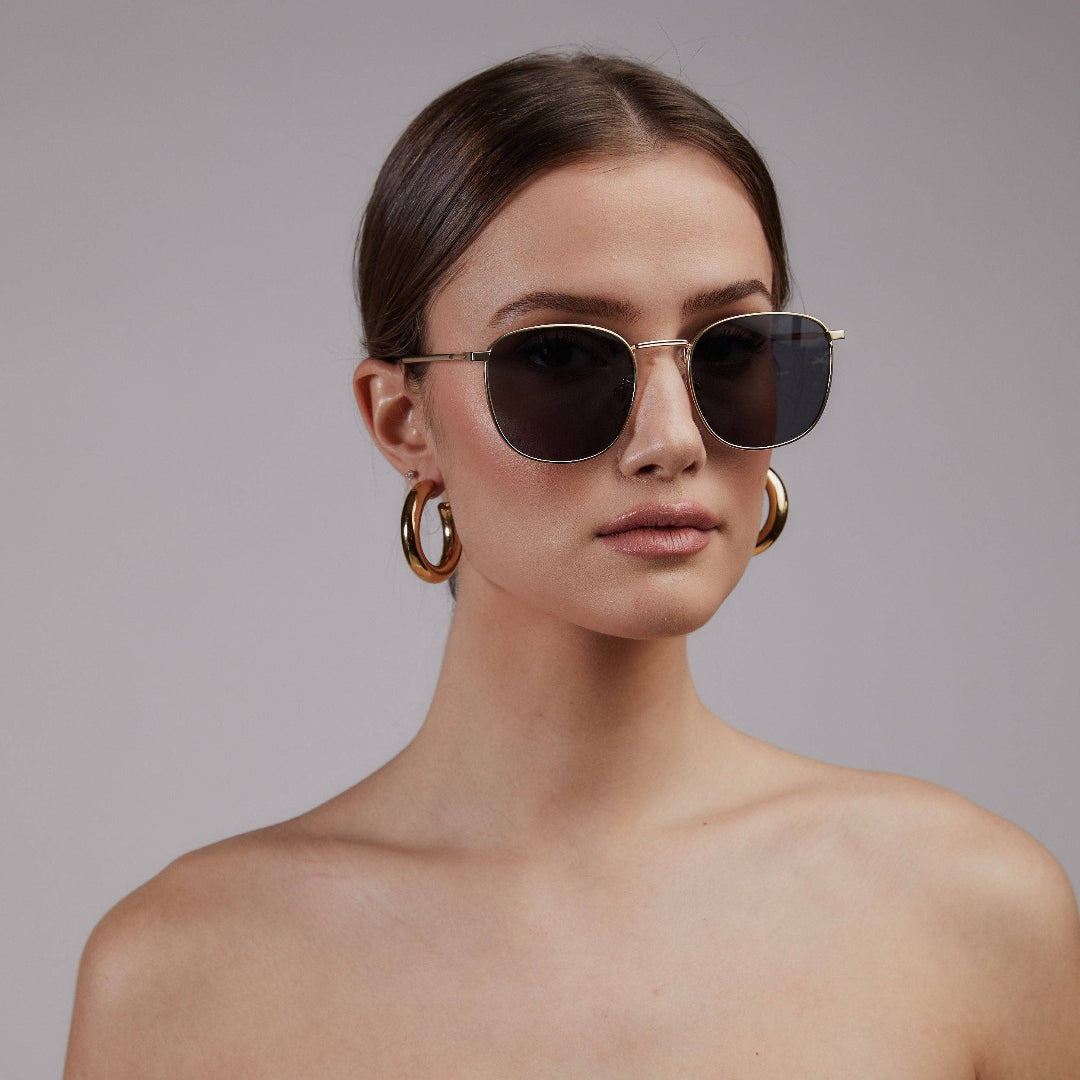 Woman wearing sunglasses and gold hoop earrings against a gray background