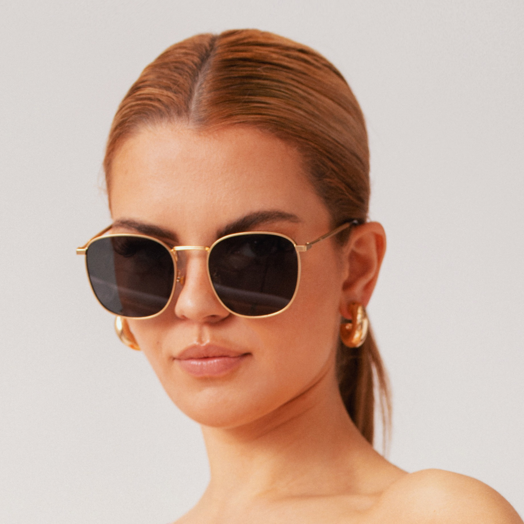 Woman wearing gold-framed sunglasses with a plain background