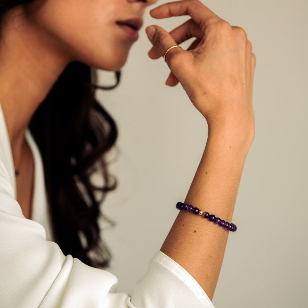 Woman wearing a white shirt with a purple beaded bracelet on a neutral background