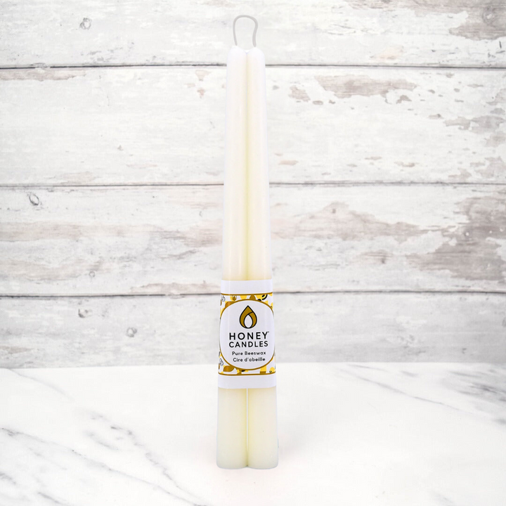 Two cream-colored beeswax candles are standing upright, tied together with a string. The candles have a label that says 