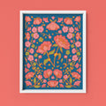 Framed floral artwork with pink flowers on a blue background against a coral wall.