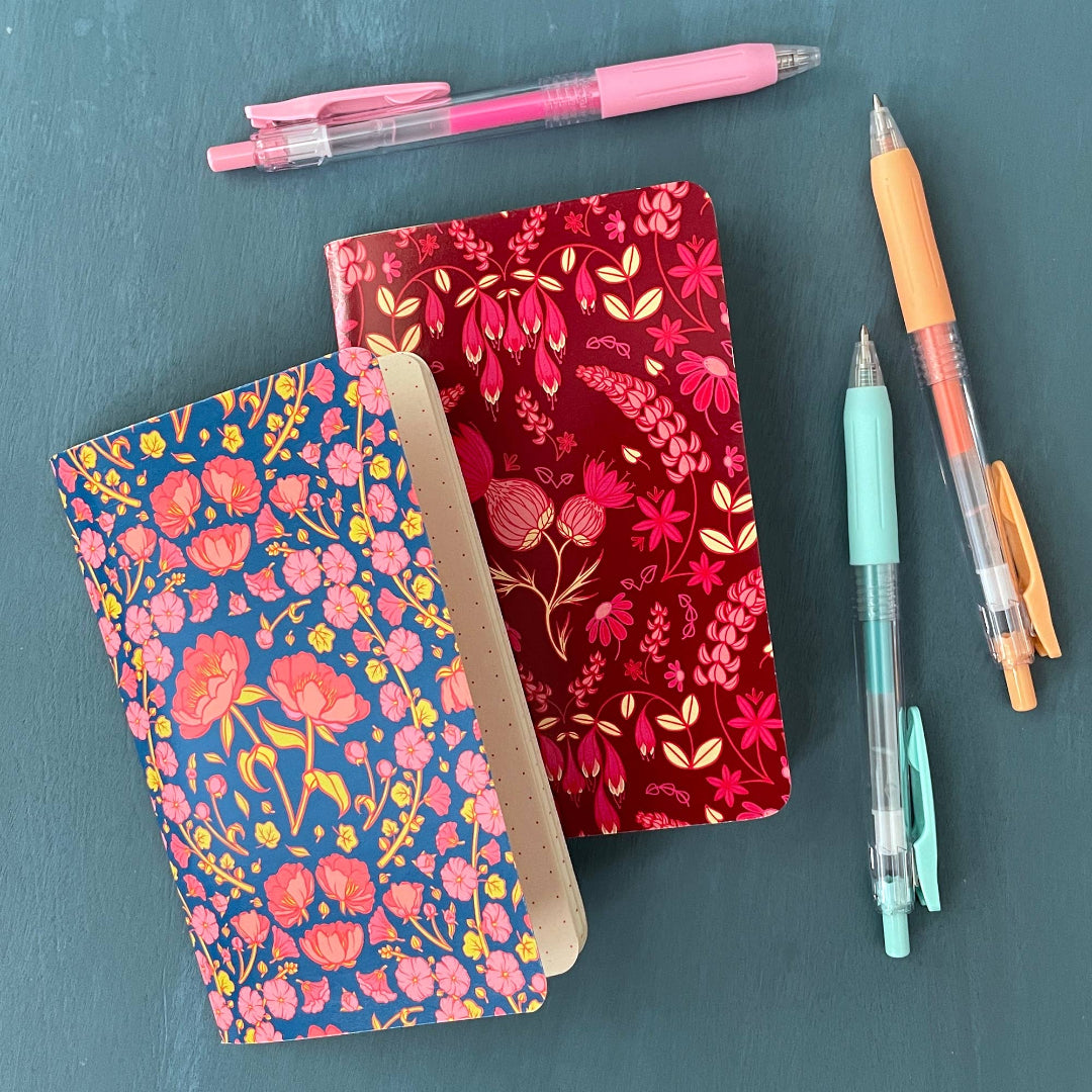 Two floral notebooks with pens on a teal background