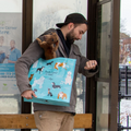 A reusable tote bag with a playful dog-themed design. The bag is a light blue color with black handles. It features a variety of dog breeds in different poses, including a bulldog, a poodle, a dachshund, and a husky. The text "People I want to meet: 1. Dogs" is printed on the bag in black.