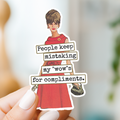 Sticker with a woman in a red dress and text held by a hand against a blurred background