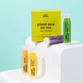 A set of four Epic Blend vegan lip balms in a yellow box. The lip balms are in different colors and flavors: peach, pineapple mint, wild berry, and coconut lemon. The box has the text "Plant One On Me" and "Vegan Lip Balms" written on it.