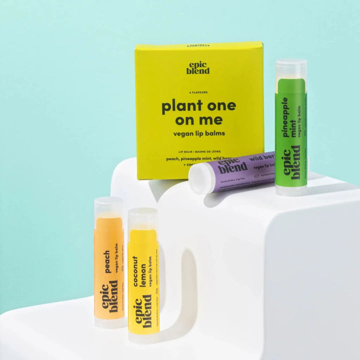 A set of four Epic Blend vegan lip balms in a yellow box. The lip balms are in different colors and flavors: peach, pineapple mint, wild berry, and coconut lemon. The box has the text 