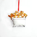 A close-up, high-angle flat lay shot on a plain white background features a soft, plush Christmas ornament shaped like a serving of poutine. The illustration shows a white cup filled with golden-brown french fries and a small amount of gravy or cheese curds. A red polka-dot ribbon loop is attached to the top for hanging.
