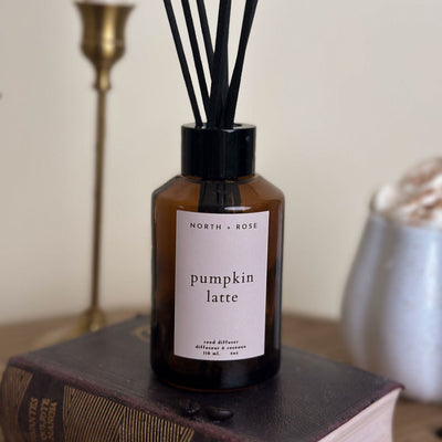 Diffuser bottle labeled 'Pumpkin Latte' by North + Rose on a book with a blurred background.