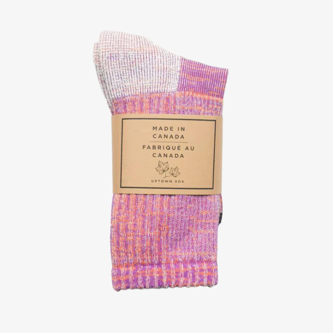 A pair of colorful socks rolled up and packaged with a label that reads "Made in Canada" and "Uptown Sox." The socks are a mix of purple, pink, and white, creating a vibrant pattern.