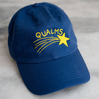 Blue cap with 'QUALMS' and a star design on a gray surface
