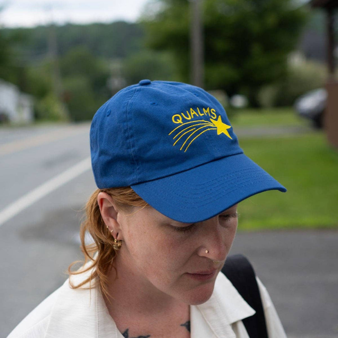 Person wearing a blue cap with a logo, standing outdoors on a road.