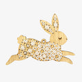 A wooden rabbit ornament embroidered with white snowflake patterns. The rabbit is depicted as leaping, with its body angled upwards and its legs stretched out.
