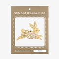 A wooden rabbit ornament embroidered with white snowflake patterns. The rabbit is depicted as leaping, with its body angled upwards and its legs stretched out.