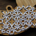 A wooden rabbit ornament embroidered with white snowflake patterns. The rabbit is depicted as leaping, with its body angled upwards and its legs stretched out.