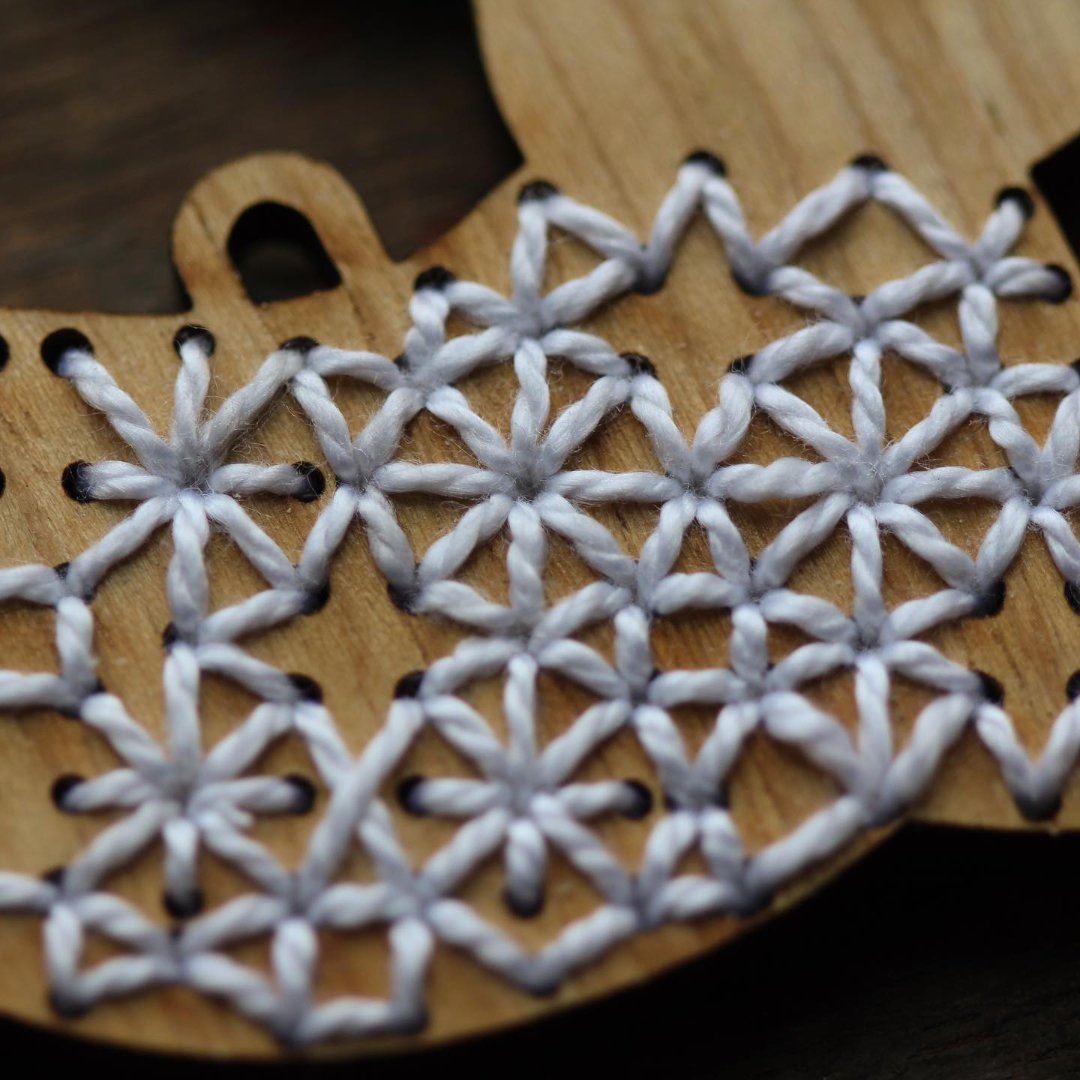 A wooden rabbit ornament embroidered with white snowflake patterns. The rabbit is depicted as leaping, with its body angled upwards and its legs stretched out.