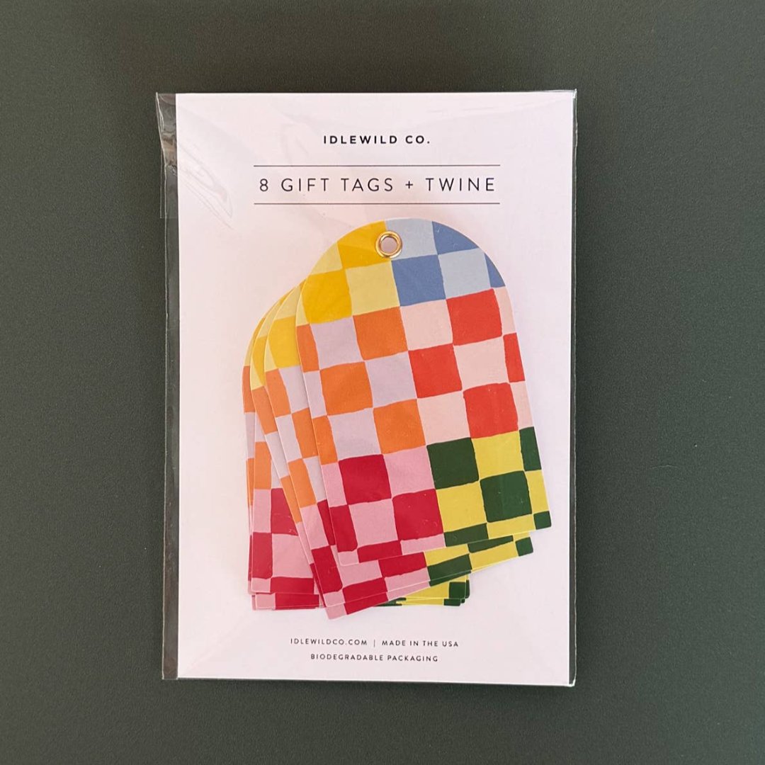A package of 8 gift tags and twine. The tags feature a colorful checkered pattern in pink, yellow, blue, and green. The packaging is white with the Idlewild Co. logo and information about the product.