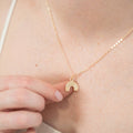 Gold necklace with a rainbow pendant worn by a person