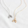 Two rainbow-shaped pendants on gold and silver necklaces against a white background