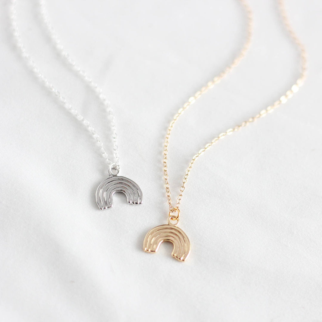 Two rainbow-shaped pendants on gold and silver necklaces against a white background