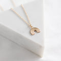 Gold necklace with a rainbow pendant on a light gray background