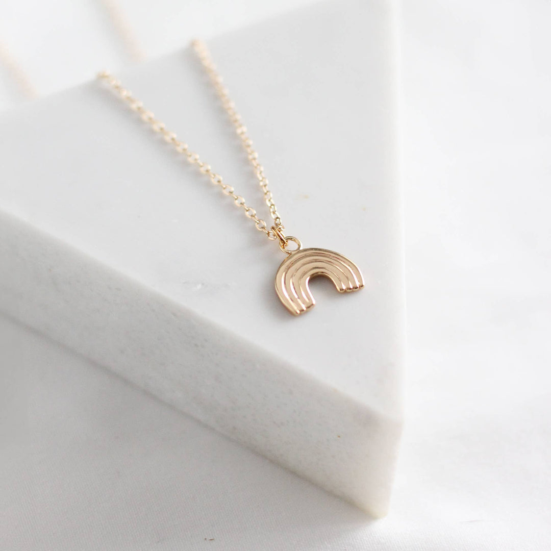 Gold necklace with a rainbow pendant on a light gray background