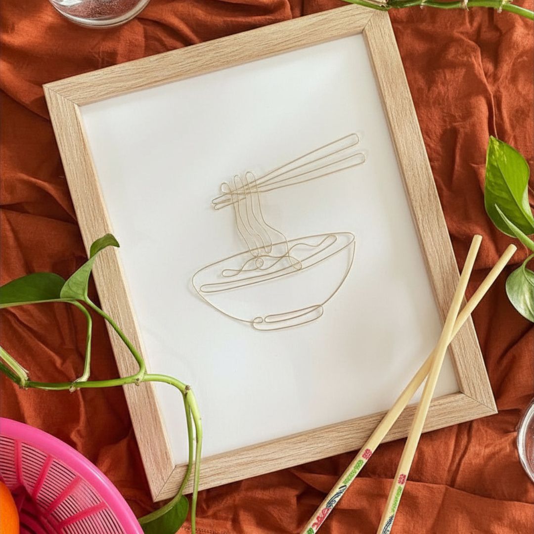 Framed artwork of a bowl with noodles and chopsticks on an orange fabric background