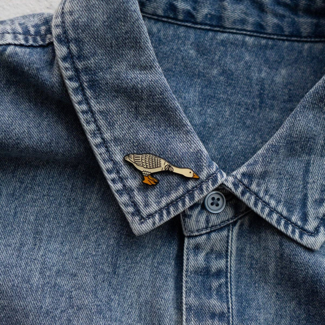 Close-up of a denim shirt collar with a decorative pin on a textured surface