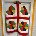 Colorful quilt with geometric patterns displayed on a white wall.