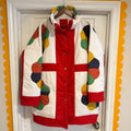 Colorful quilt with geometric patterns displayed on a white frame against a yellow and white scalloped border.