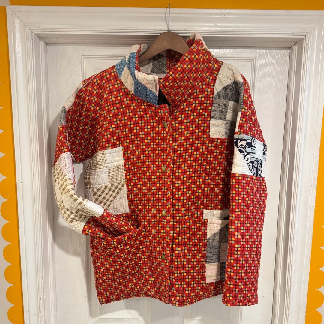 A patchwork quilted jacket hanging on a wooden hanger against a white door, featuring a red and yellow patterned body with beige, blue, and gray patchwork details.