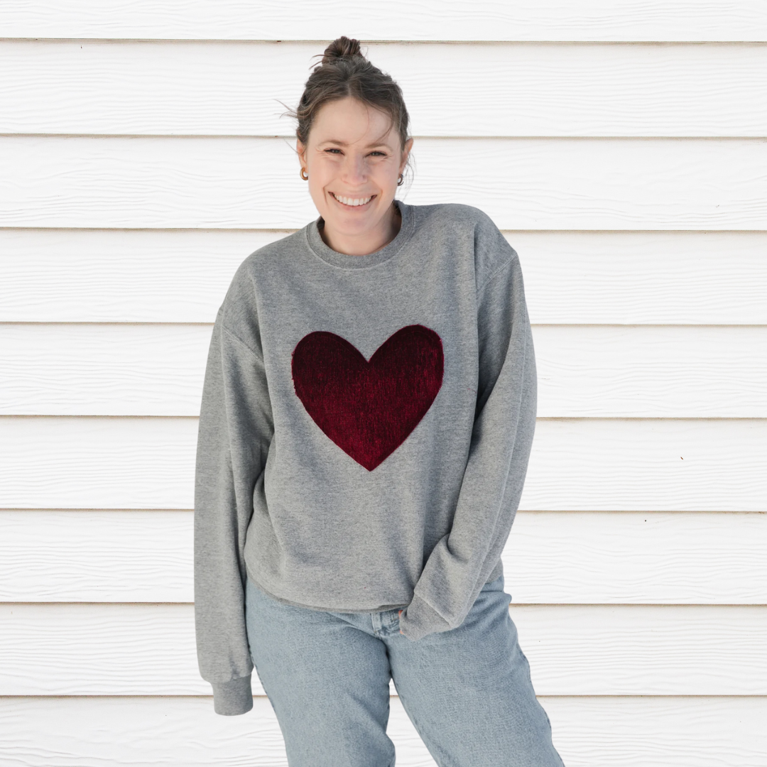 Person wearing a gray sweatshirt with a red heart design against a white wall.