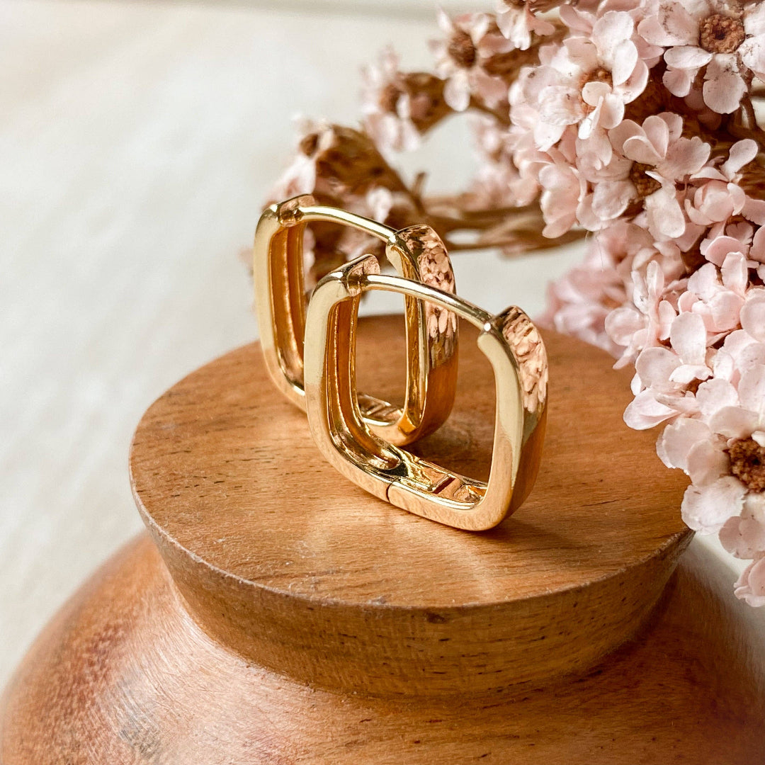 Gold hoop earrings on a wooden stand with pink flowers in the background