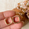 Gold hoop earrings held between fingers with dried flowers in the background