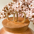 Gold hoop earrings on a wooden stand with pink flowers in the background