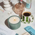 Candle, coffee cup, and other items on a table with a soft focus background