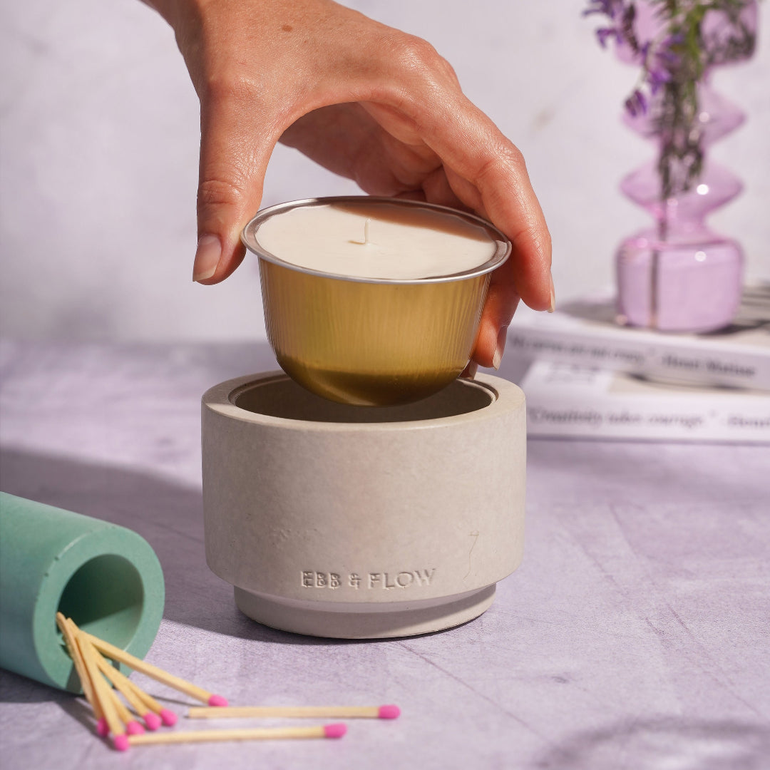 Hand placing a small candle into a gray candle warmer with matches nearby on a light surface.