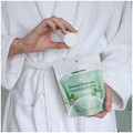 Person holding a package of Nature Bee shower steamers and a single steamers in a white robe.