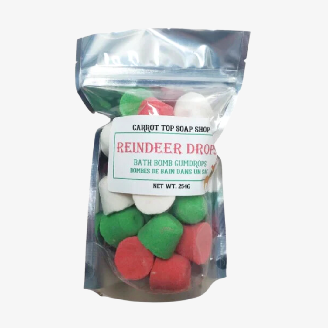 A resealable plastic bag filled with colorful bath bombs. The bath bombs are shaped like gumdrops in red, white, and green. The bag has a label that reads "Carrot Top Soap Shop" and "Reindeer Drops Bath Bomb Gumdrops."