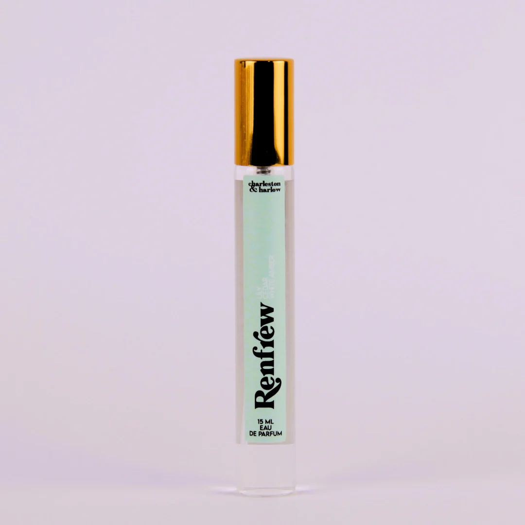 A bottle of Charleston & Harlow perfume named "Renfrew." The bottle is clear glass with a gold spray cap. The label is light green with the brand name and perfume name in a bold, playful font. The fragrance notes are listed as "Lily, Cedar, White Amber."