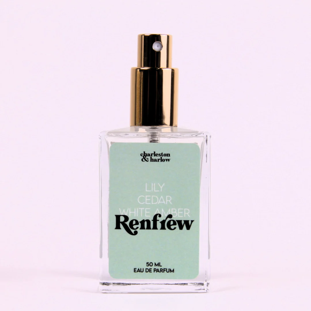 A bottle of Charleston & Harlow perfume named "Renfrew." The bottle is clear glass with a gold spray cap. The label is light green with the brand name and perfume name in a bold, playful font. The fragrance notes are listed as "Lily, Cedar, White Amber."