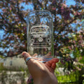 Clear glass with a Volkswagen van etching held in front of a blurred outdoor background with trees.