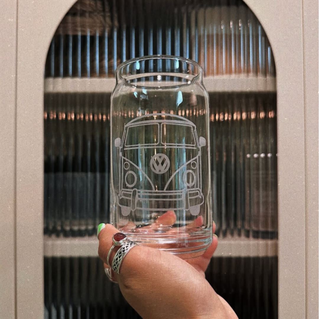 Hand holding a clear glass jar with a Volkswagen van design against a blurred indoor background