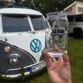 Hand holding a glass with a VW bus etching in front of a classic VW camper van.